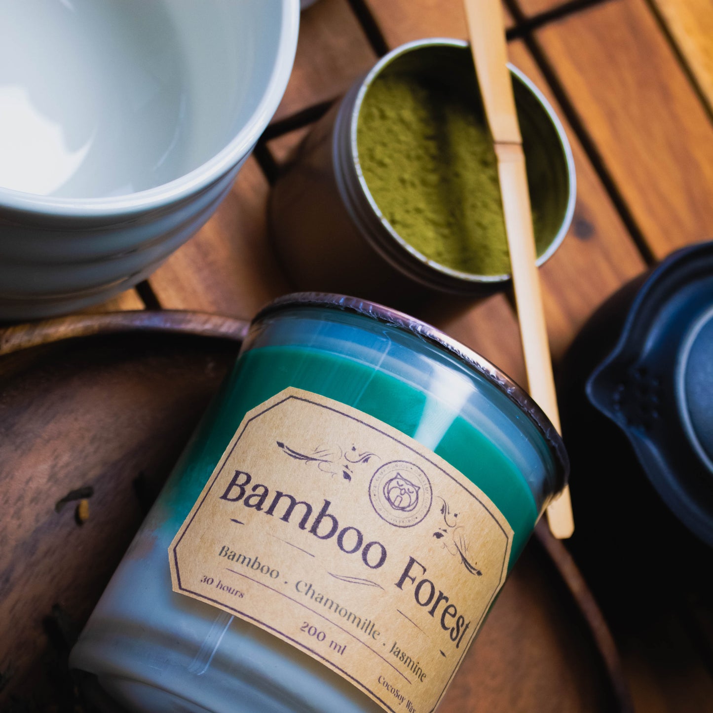 Bamboo Forest candle on a wooden surface with tea leaves and a teacup.
