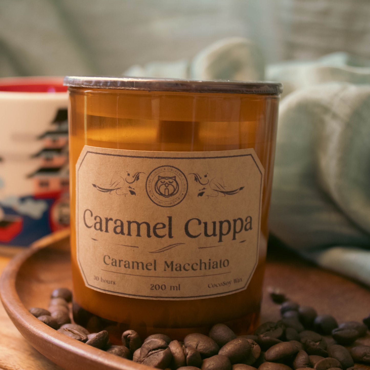 Caramel Cuppa candle on a wooden tray with coffee beans and a mug in the background