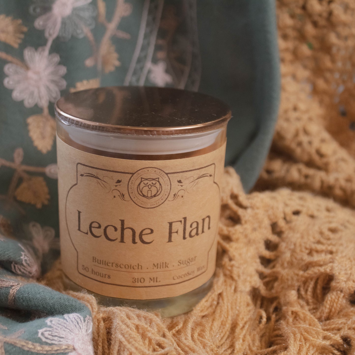 Candle labeled 'Leche Flan' on a textured fabric background