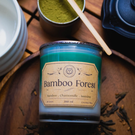 Candle labeled 'Bamboo Forest' on a wooden surface with tea leaves and a small container of green powder.