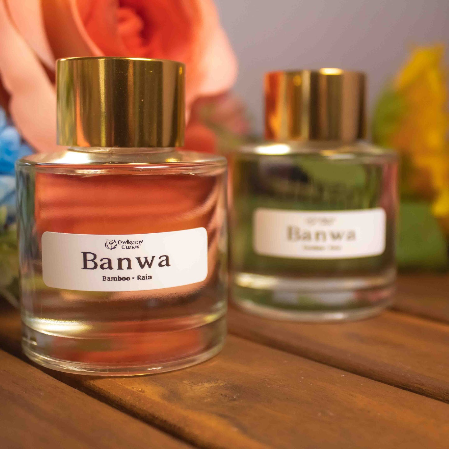 Two reed diffuser bottles labeled 'Banwa' on a wooden surface with flowers in the background.