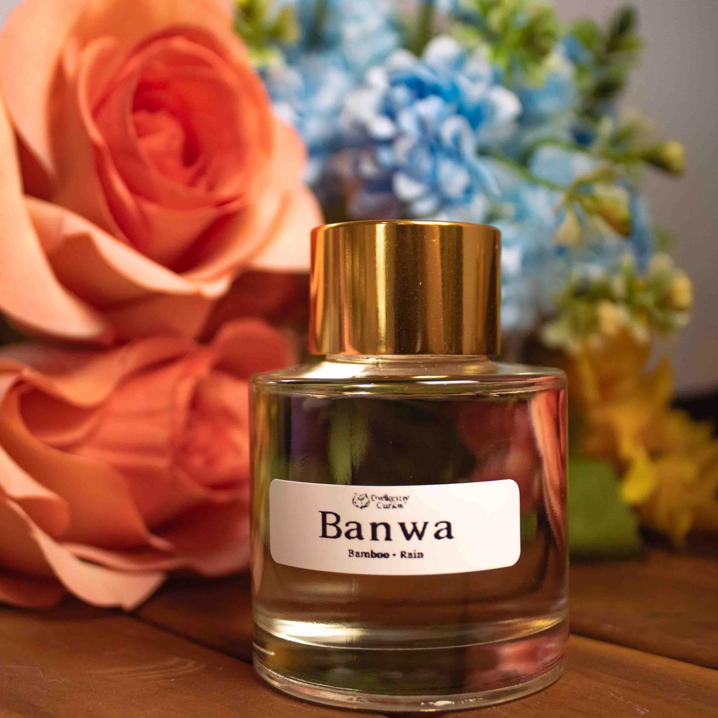 Bottle of Banwa reed diffuser with flowers in the background