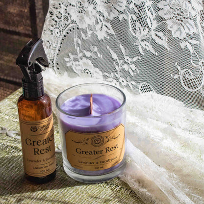 Candle and spray bottle labeled 'Greater Rest' on a textured surface with lace in the background