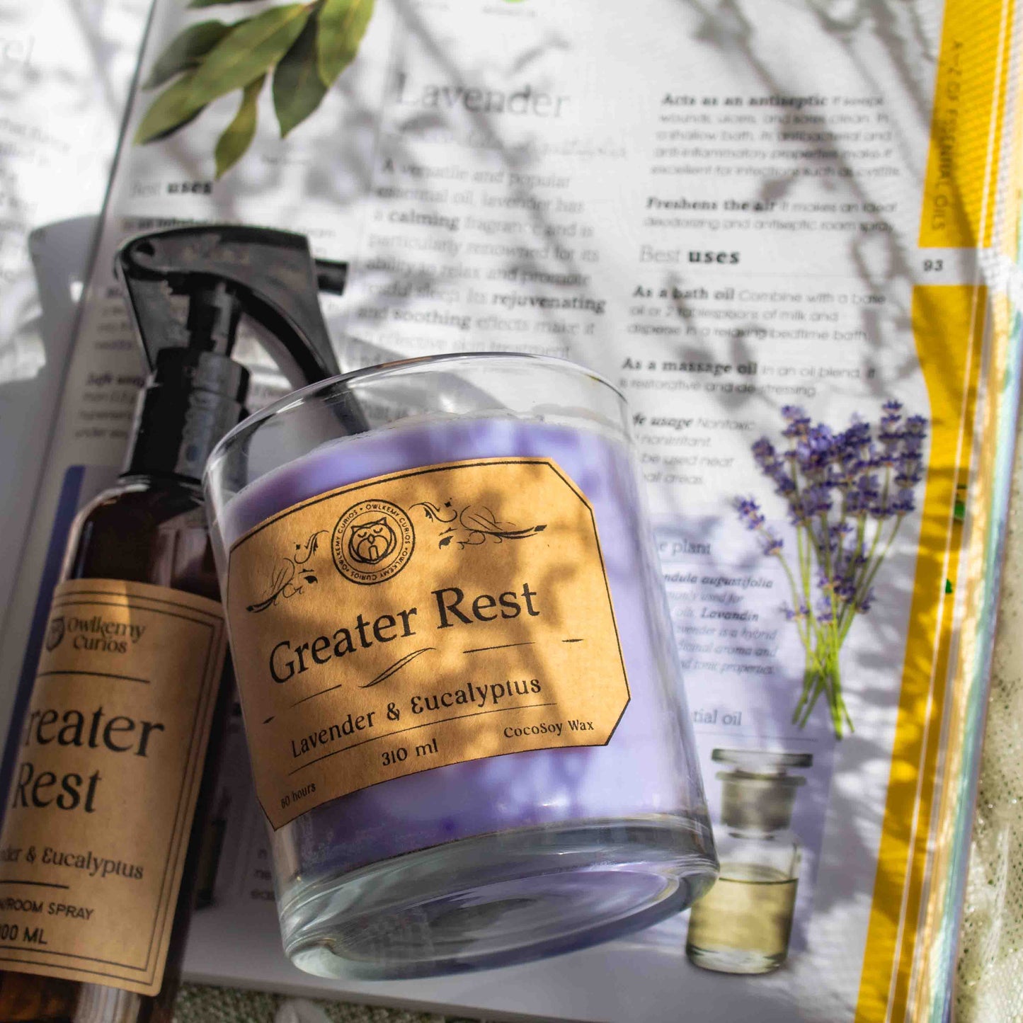 Candle and spray bottle labeled 'Greater Rest' on an open magazine with lavender imagery.