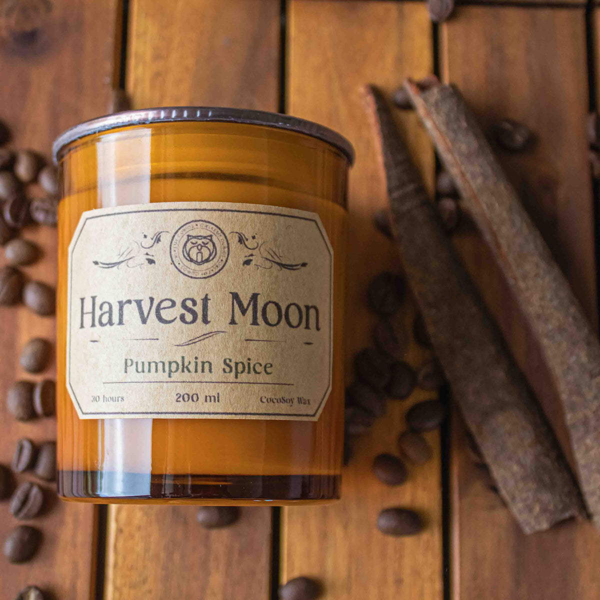 Harvest Moon Pumpkin Spice candle on a wooden surface with coffee beans and cinnamon sticks.