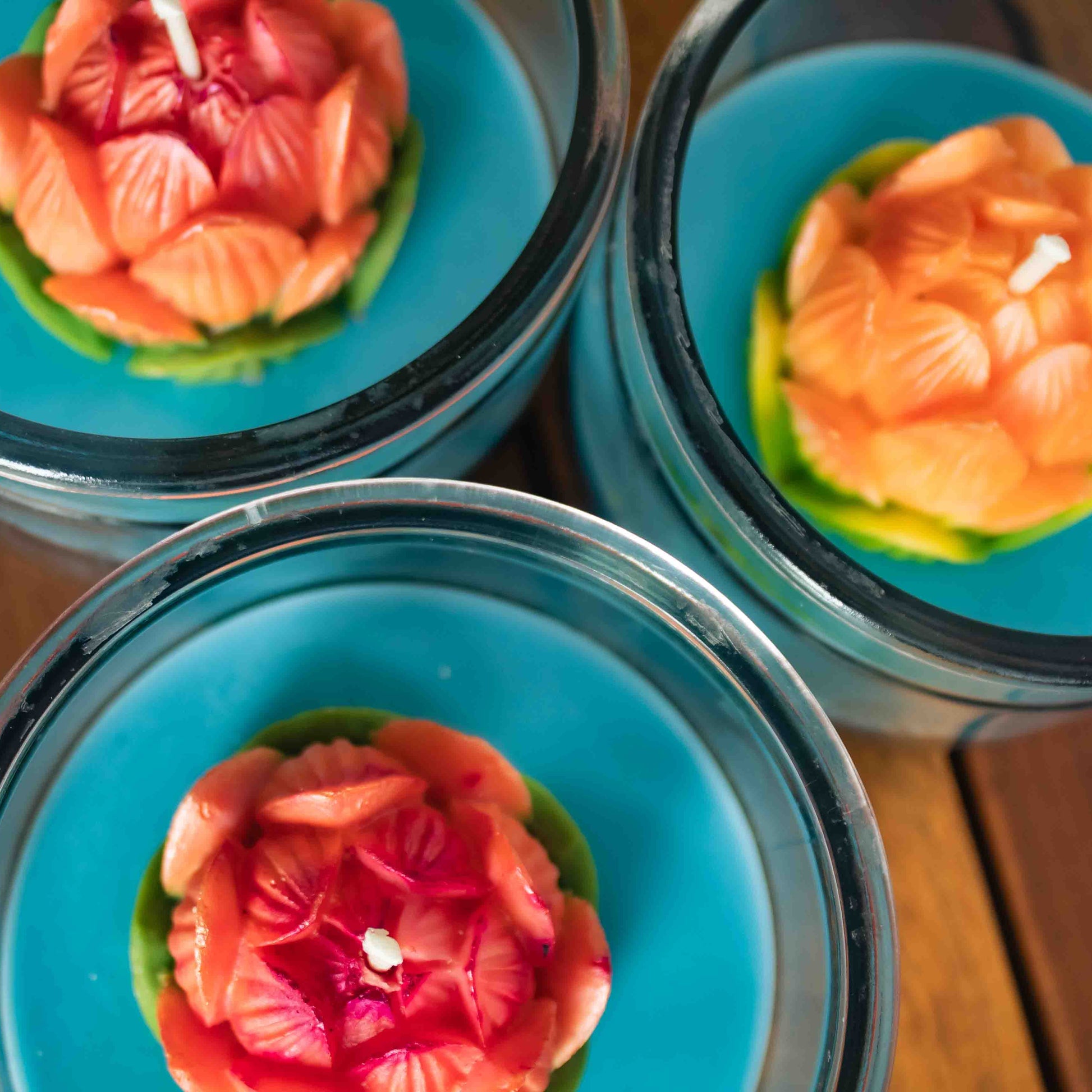 Three floral-patterned lotus candles in glass containers on a wooden surface