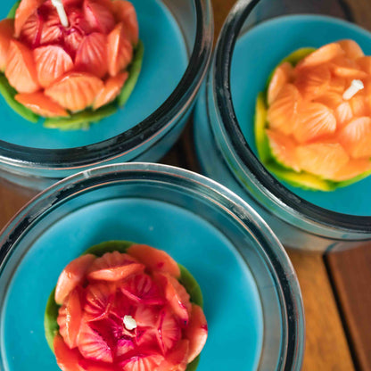 Three floral-patterned lotus candles in glass containers on a wooden surface