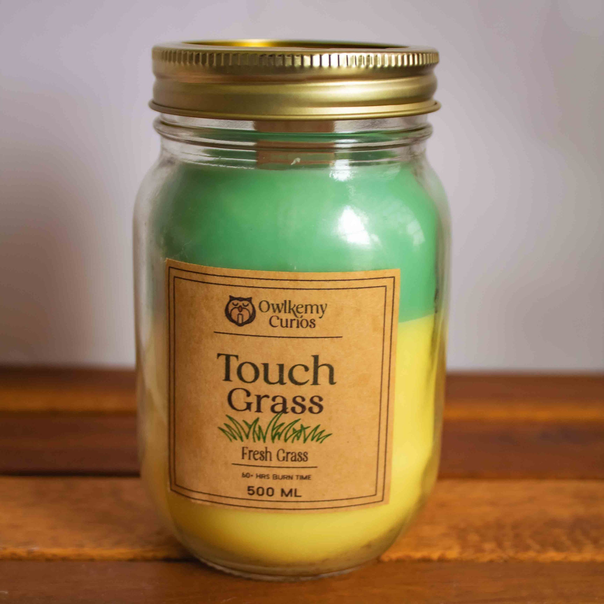 Jar of 'Touch Grass' candle with a gold lid on a wooden surface