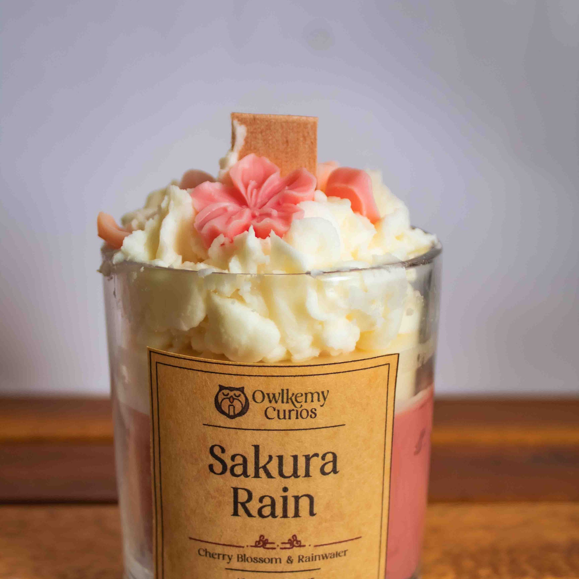 Candle labeled 'Sakura Rain' with decorative elements on a wooden surface
