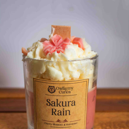 Candle labeled 'Sakura Rain' with decorative elements on a wooden surface