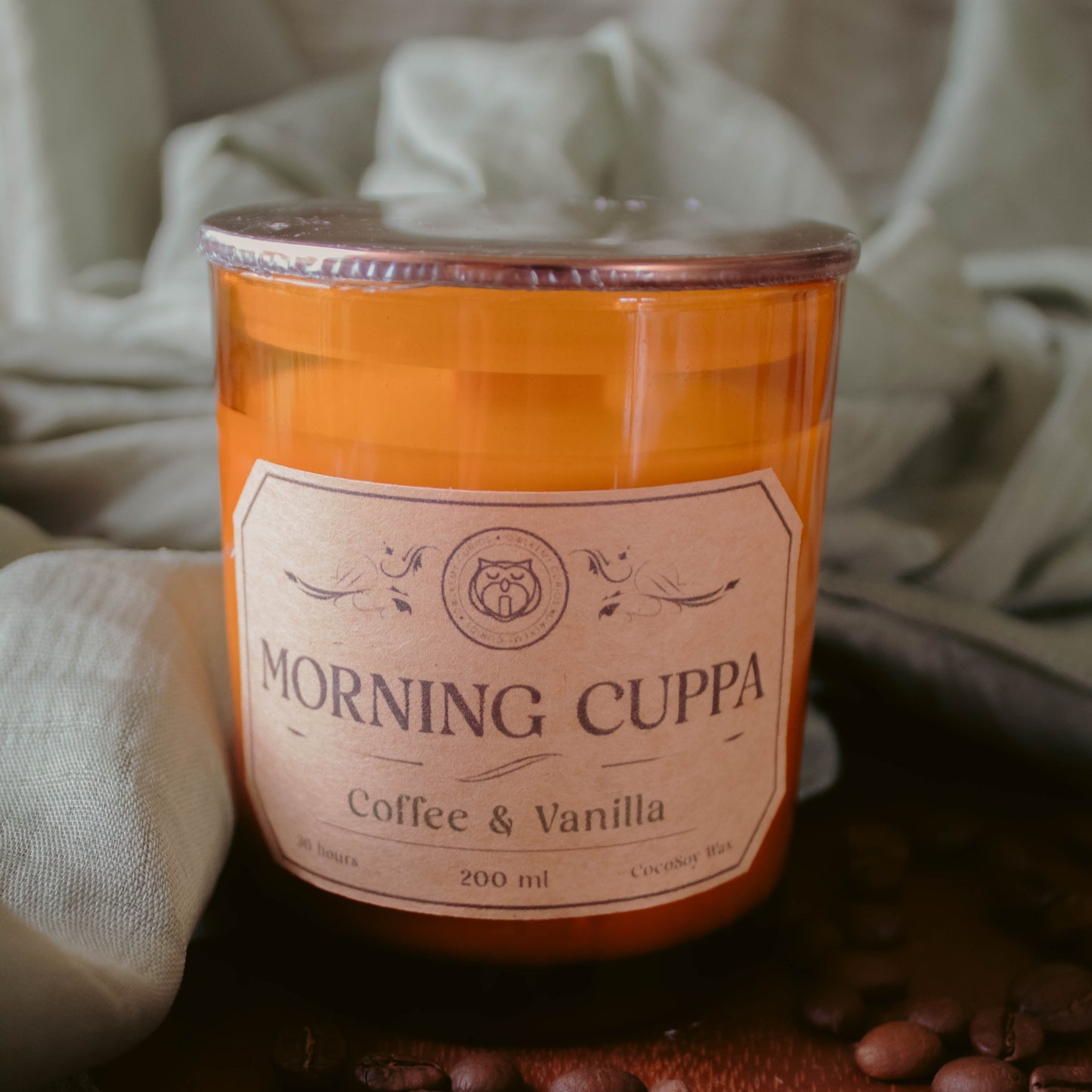 Candle labeled 'Morning Cuppa Coffee & Vanilla' with coffee beans on a wooden surface.